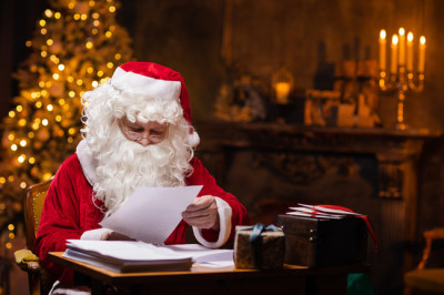 Weihnachtsmann liest Wunschzettel am Schreibtisch – jetzt Weihnachtsmann mieten für Events und Firmenfeiern