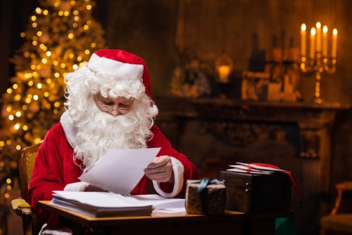 Weihnachtsmann liest Wunschzettel am Schreibtisch – jetzt Weihnachtsmann mieten für Events und Firmenfeiern